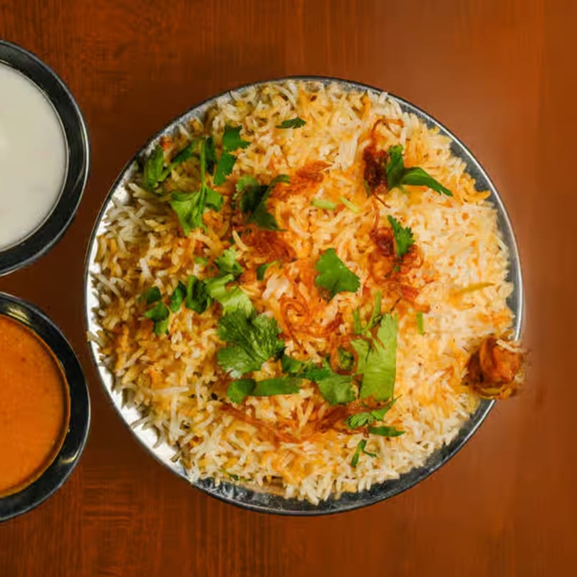 Indian chicken biryani with rice, cilantro, and fried onions, served with two side sauces.