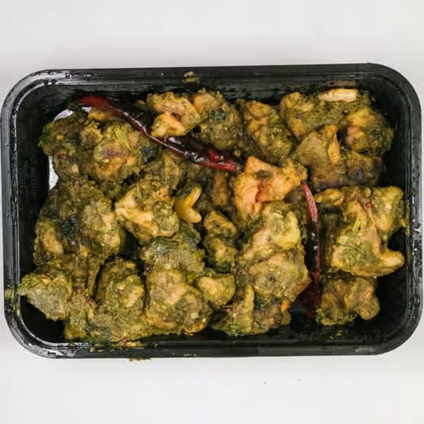 UlavacharU Indian Restaurant's green chicken curry with red chilies in a black container.