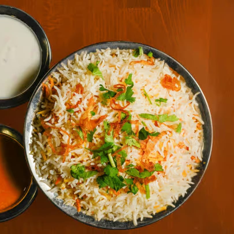 A bowl of Indian biryani rice with fried onions and cilantro, served with two sauces.