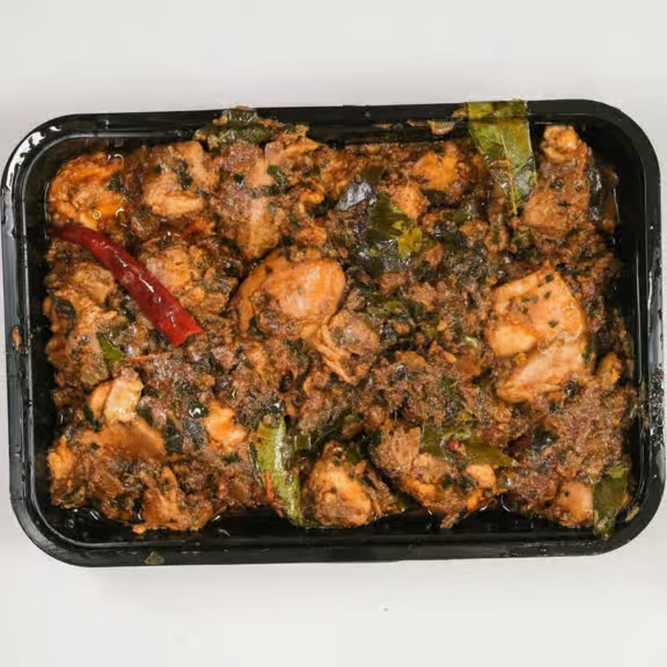 UlavacharU Indian Restaurant's chicken curry, rich with spices and green herbs, in a black container.