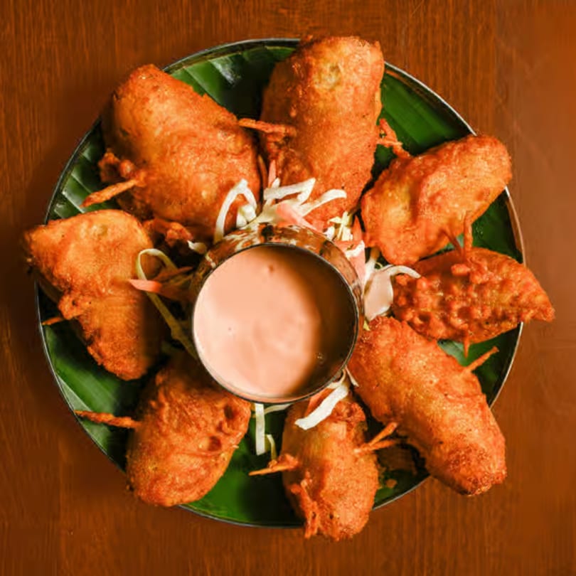 Crispy fried Indian chicken lollipops arranged around a bowl of pink dipping sauce on a banana leaf.