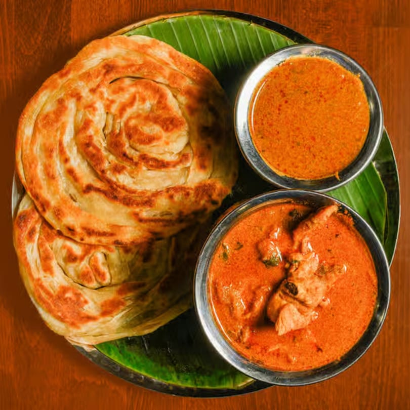 Indian parotta bread and two bowls of chicken curry on a banana leaf.